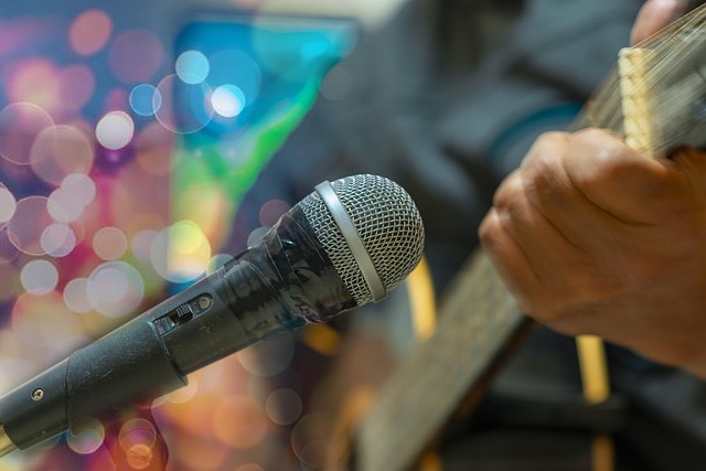 Close-up of a microphone and a person playing a guitar with colorful bokeh lights in the background